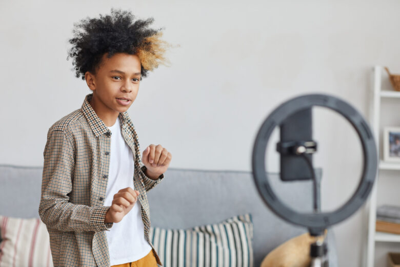 Academy of Acting Waist up portrait of teenage African-American boy dancing to camera set on ringlight at home, young blogger concept, copy space