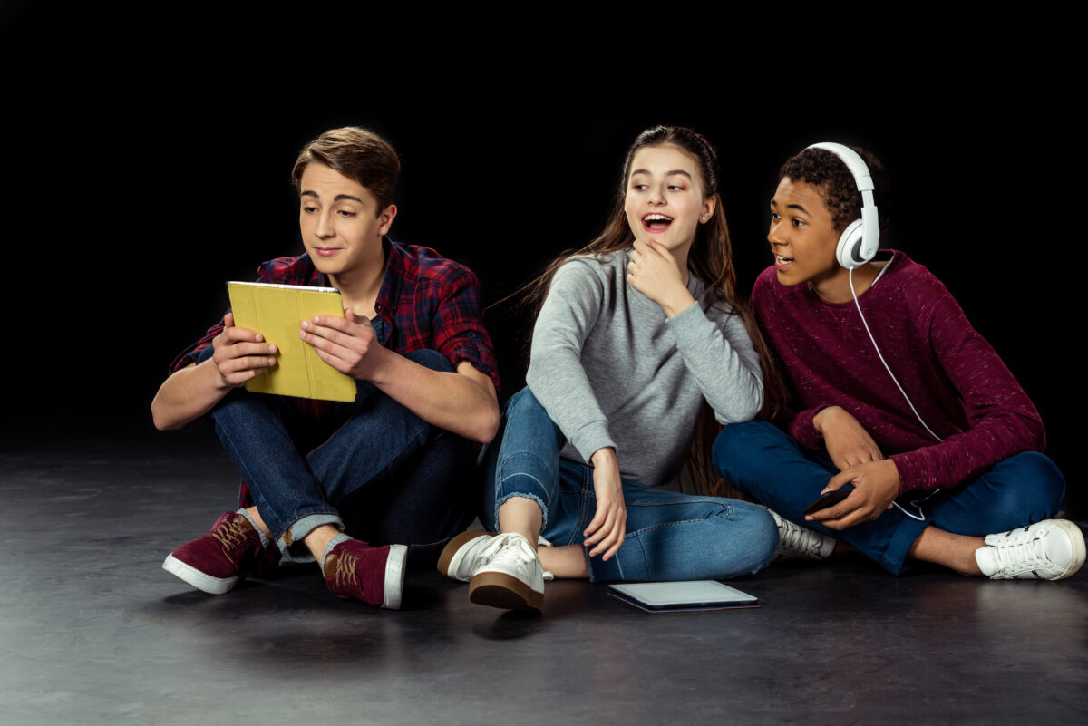 Academy of Acting teenagers interested looking at friend using tablet on black