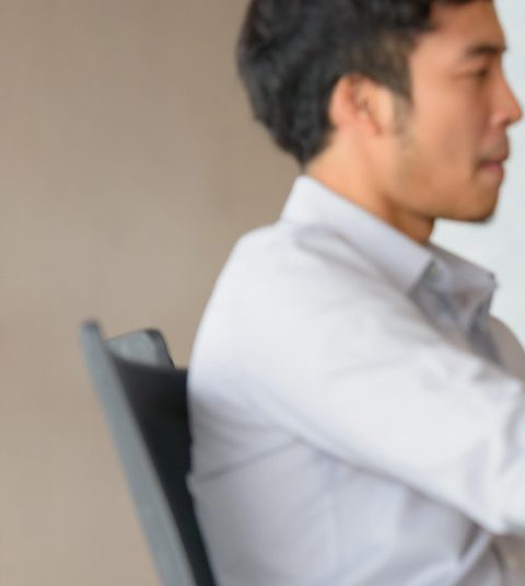A man sitting in a chair with his arm resting on the back of another person.